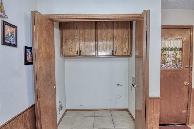 laundry area with wooden walls, light tile patterned floors, and a textured ceiling