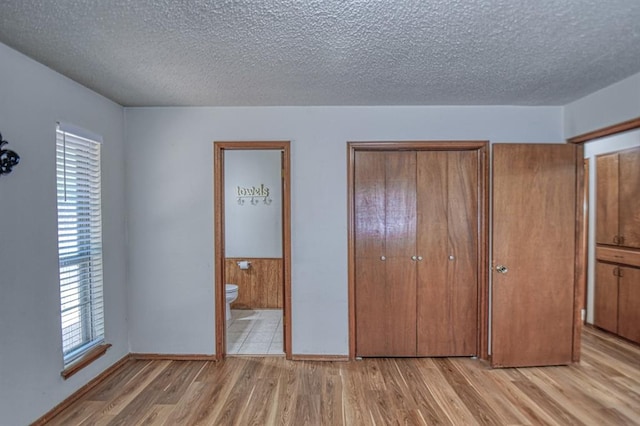 unfurnished bedroom with ensuite bathroom, light hardwood / wood-style floors, and a textured ceiling