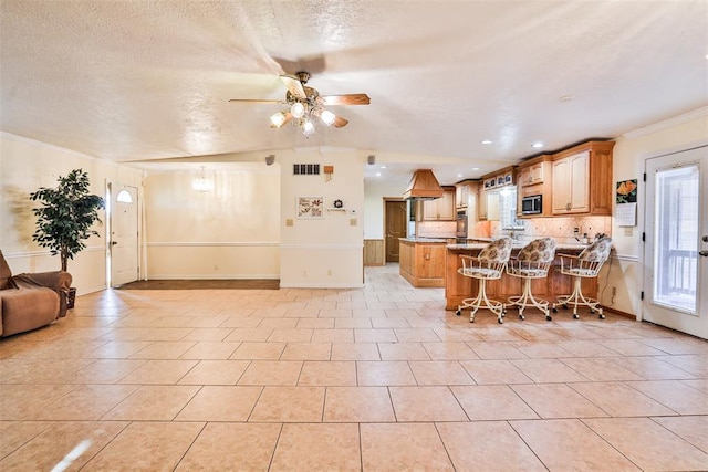 kitchen with backsplash, kitchen peninsula, crown molding, a kitchen bar, and light tile patterned floors