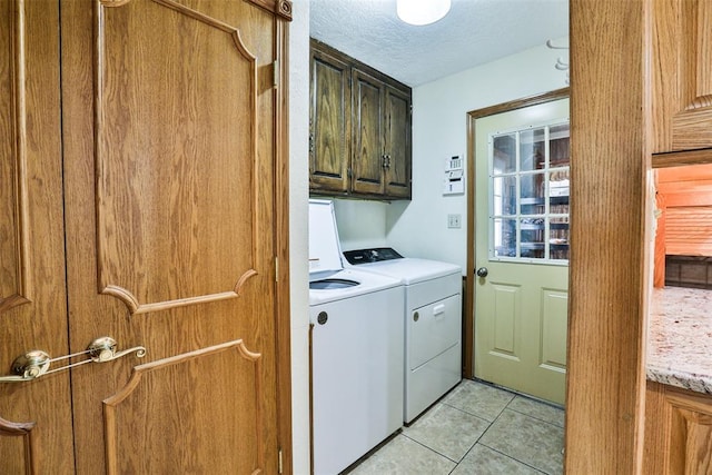 laundry area with light tile patterned flooring, cabinets, a textured ceiling, and washing machine and clothes dryer