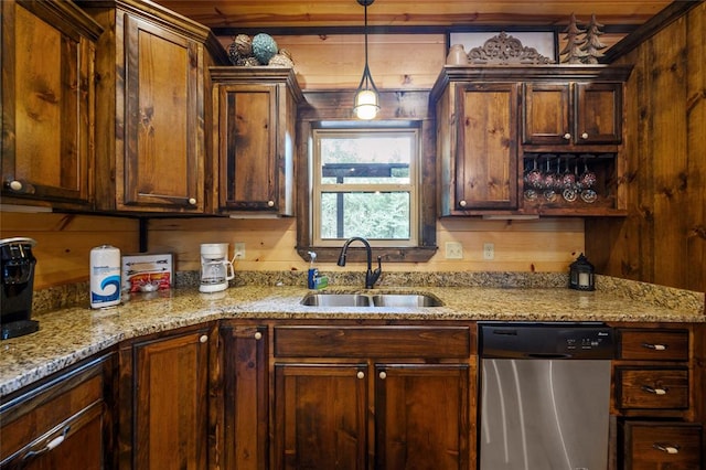 kitchen featuring pendant lighting, dishwasher, sink, wooden walls, and light stone countertops