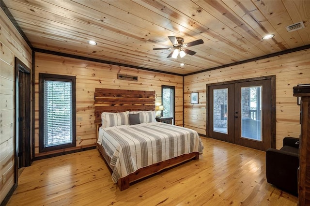 bedroom with french doors, light hardwood / wood-style flooring, ceiling fan, and wood walls