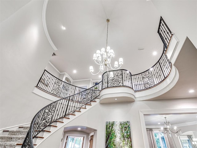 stairway with a towering ceiling, an inviting chandelier, and crown molding