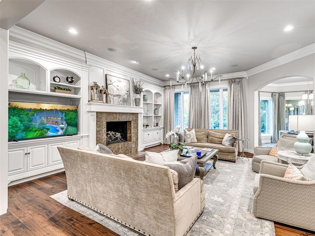 living room with an inviting chandelier, built in features, crown molding, hardwood / wood-style floors, and a fireplace