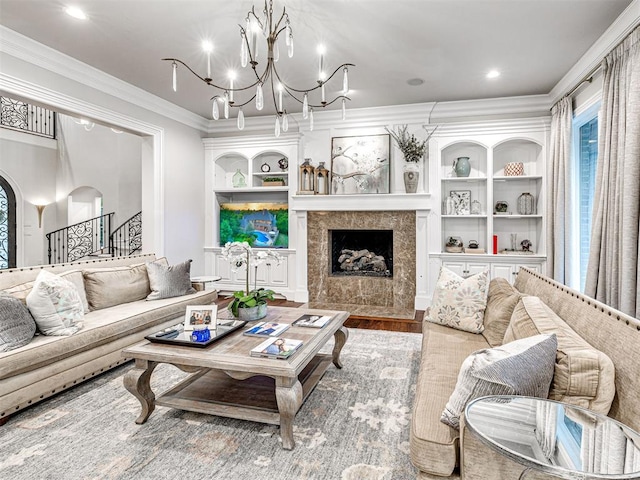 living room with built in shelves, a chandelier, wood-type flooring, a tiled fireplace, and ornamental molding