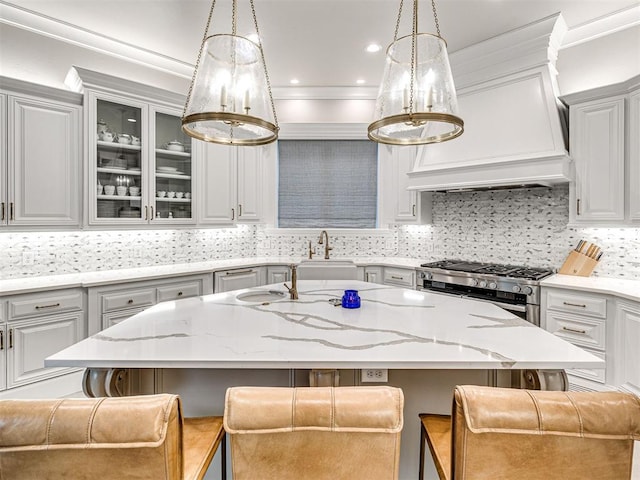 kitchen with decorative backsplash, premium range hood, a breakfast bar, high end stainless steel range oven, and an island with sink