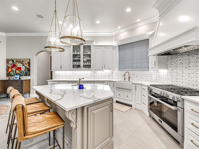 kitchen featuring decorative backsplash, light tile patterned floors, high end stove, and an island with sink