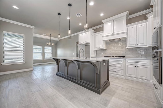 kitchen featuring appliances with stainless steel finishes, a breakfast bar, pendant lighting, white cabinets, and an island with sink