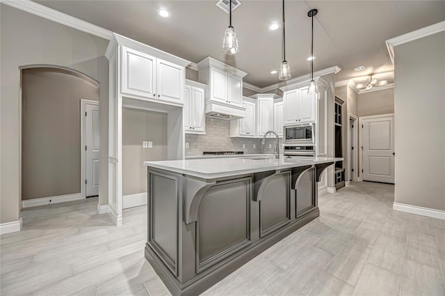 kitchen featuring appliances with stainless steel finishes, decorative light fixtures, white cabinetry, and an island with sink