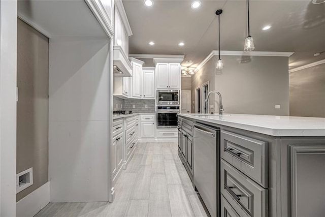 kitchen with backsplash, crown molding, an island with sink, white cabinets, and appliances with stainless steel finishes