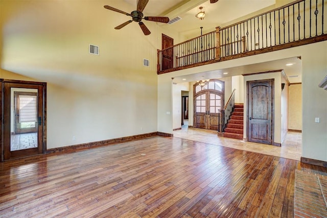 unfurnished living room with beam ceiling, wood-type flooring, a towering ceiling, and french doors