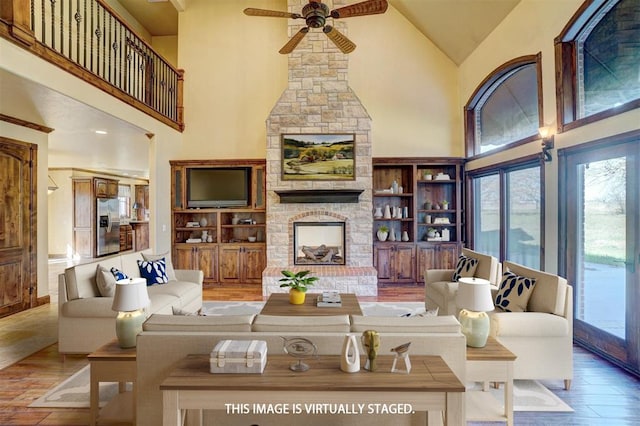 living room with high vaulted ceiling, hardwood / wood-style flooring, ceiling fan, built in features, and a fireplace