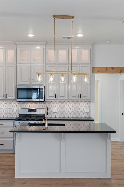 kitchen with backsplash, white cabinets, a center island with sink, sink, and appliances with stainless steel finishes