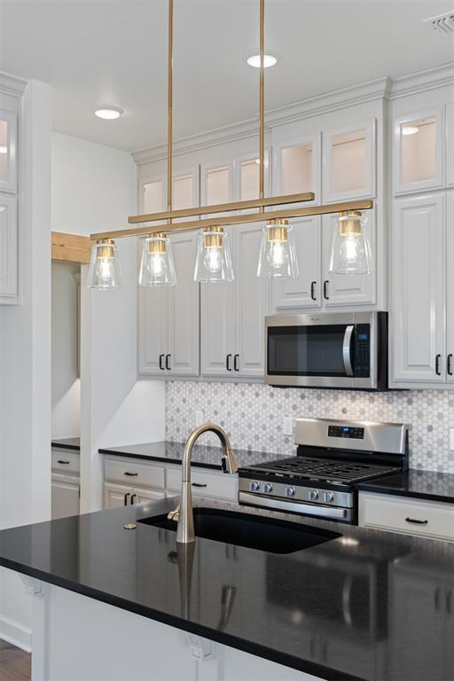 kitchen featuring decorative backsplash, appliances with stainless steel finishes, white cabinetry, and pendant lighting