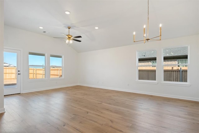 spare room featuring ceiling fan with notable chandelier, light wood-type flooring, and lofted ceiling