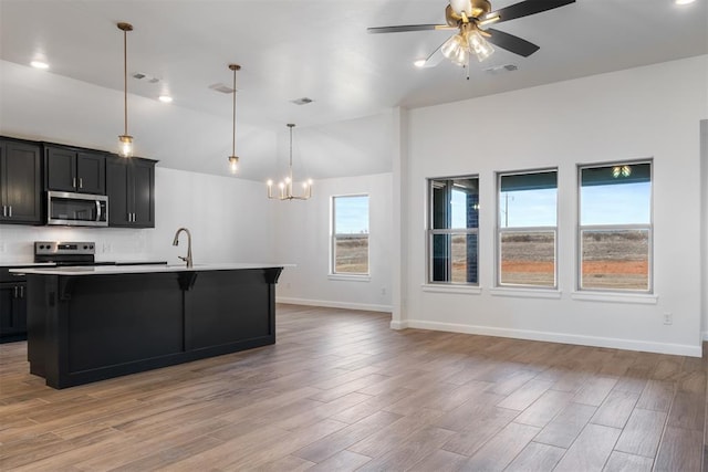 kitchen featuring ceiling fan with notable chandelier, stainless steel appliances, a kitchen island with sink, pendant lighting, and light hardwood / wood-style flooring