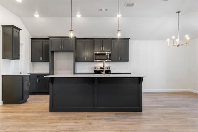 kitchen with stainless steel appliances, a notable chandelier, an island with sink, pendant lighting, and lofted ceiling