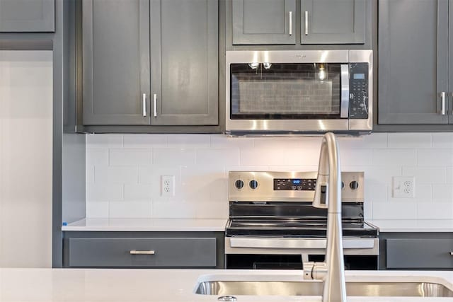 kitchen with tasteful backsplash, gray cabinets, and appliances with stainless steel finishes