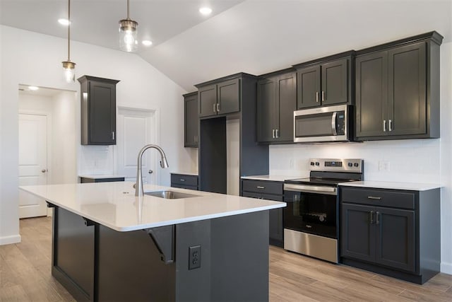 kitchen with stainless steel appliances, sink, pendant lighting, a center island with sink, and light hardwood / wood-style flooring