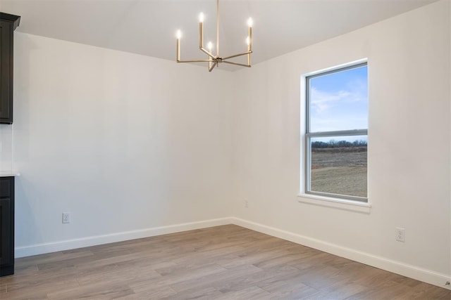 unfurnished dining area with a notable chandelier, a wealth of natural light, and light hardwood / wood-style flooring