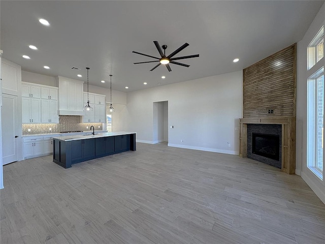 kitchen with white cabinets, hanging light fixtures, ceiling fan, light wood-type flooring, and an island with sink