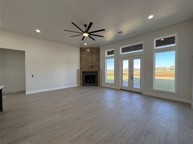 unfurnished living room featuring ceiling fan, a fireplace, french doors, and light wood-type flooring