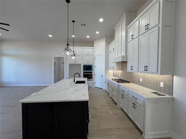 kitchen with white cabinetry, sink, light hardwood / wood-style floors, a spacious island, and appliances with stainless steel finishes