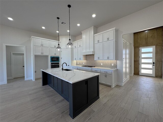 kitchen with appliances with stainless steel finishes, light stone counters, a spacious island, sink, and white cabinetry