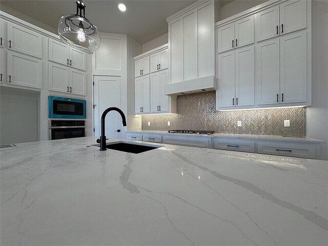 kitchen with pendant lighting, white cabinets, sink, light stone counters, and stainless steel appliances