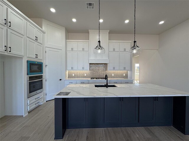 kitchen with light stone countertops, a large island with sink, decorative light fixtures, white cabinets, and oven