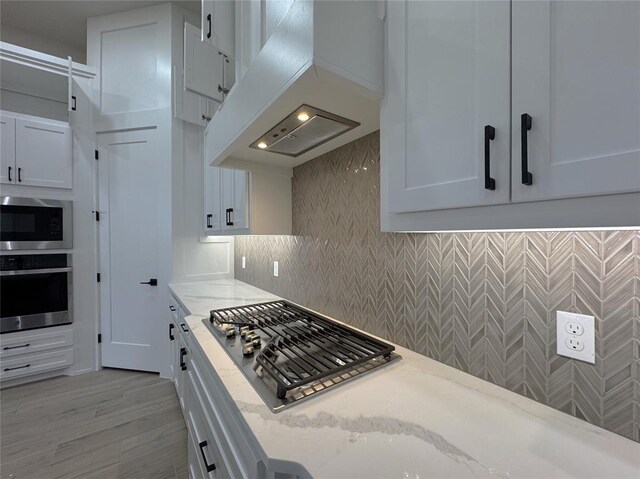 kitchen featuring backsplash, white cabinets, light stone counters, custom range hood, and stainless steel appliances