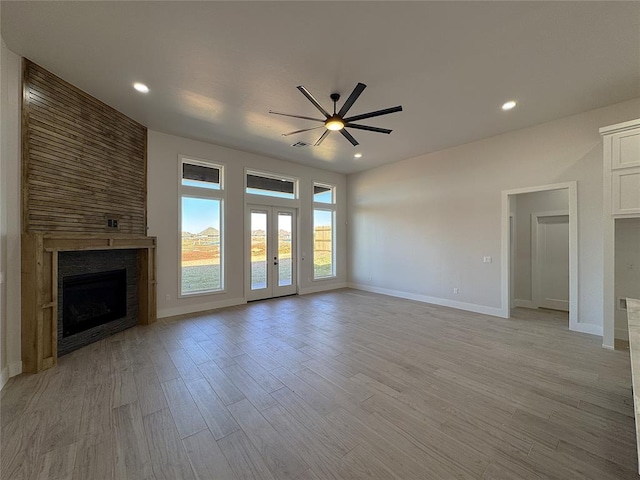 unfurnished living room with french doors, a large fireplace, light hardwood / wood-style flooring, and ceiling fan