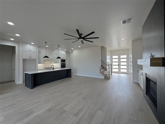 kitchen featuring white cabinetry, a large fireplace, hanging light fixtures, light hardwood / wood-style flooring, and a kitchen island with sink