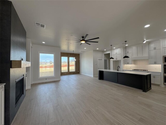 kitchen featuring light hardwood / wood-style floors, white cabinetry, ceiling fan, and an island with sink