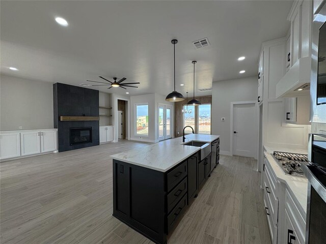 kitchen with a tile fireplace, ceiling fan, decorative light fixtures, a kitchen island with sink, and white cabinets