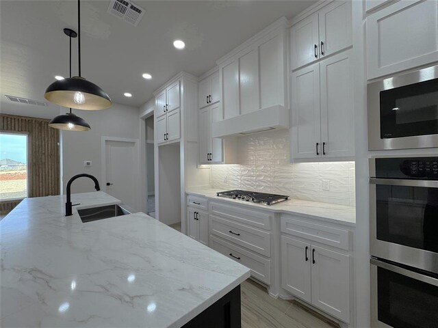 kitchen featuring white cabinets, decorative light fixtures, light stone countertops, and sink