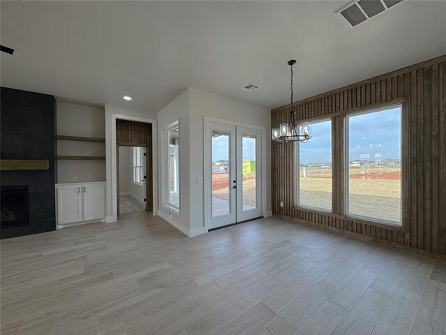 unfurnished dining area with a tile fireplace, light wood-type flooring, and a chandelier