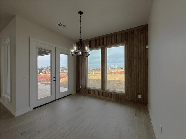 unfurnished dining area featuring light wood-type flooring, french doors, and a chandelier