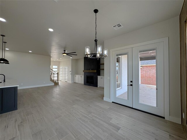 unfurnished living room featuring french doors, ceiling fan with notable chandelier, sink, light wood-type flooring, and a large fireplace