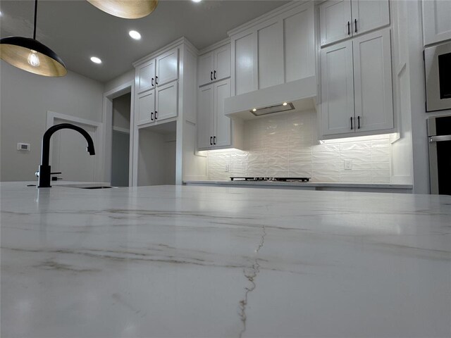 kitchen featuring stainless steel oven, white cabinets, hanging light fixtures, decorative backsplash, and light stone countertops