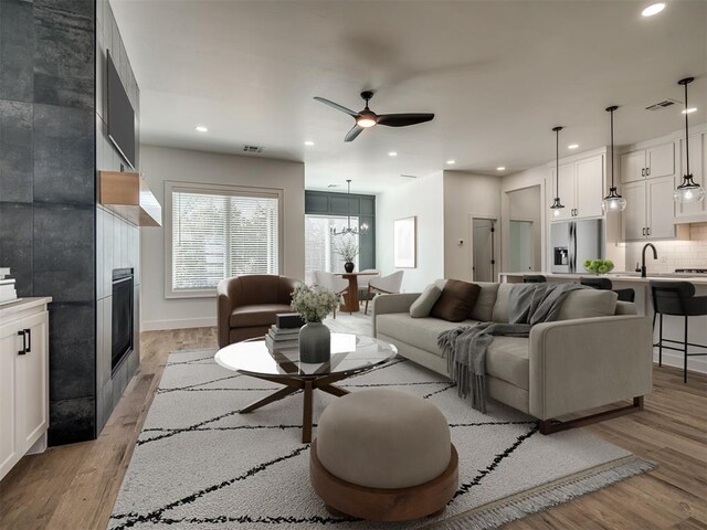 living room featuring a tile fireplace, sink, light hardwood / wood-style floors, and ceiling fan with notable chandelier