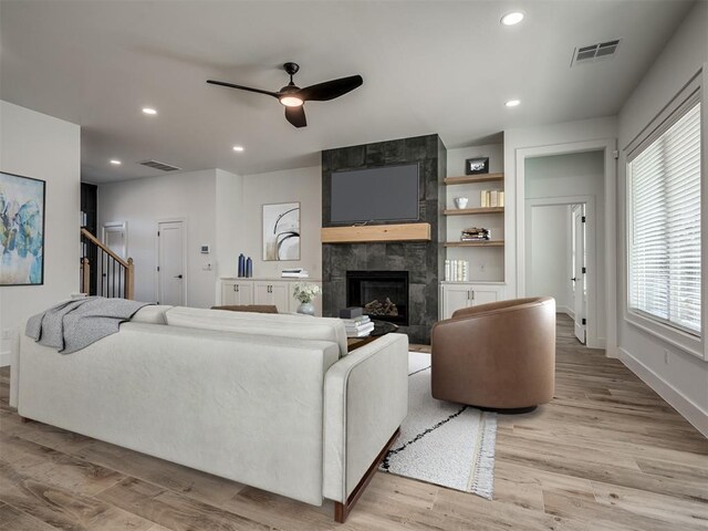 living room featuring a tiled fireplace, ceiling fan, and light wood-type flooring