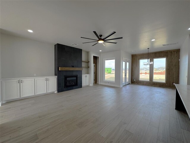 unfurnished living room with a large fireplace, light hardwood / wood-style floors, and ceiling fan with notable chandelier