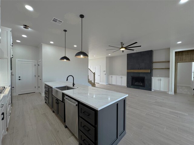 kitchen with appliances with stainless steel finishes, sink, a tile fireplace, decorative light fixtures, and an island with sink