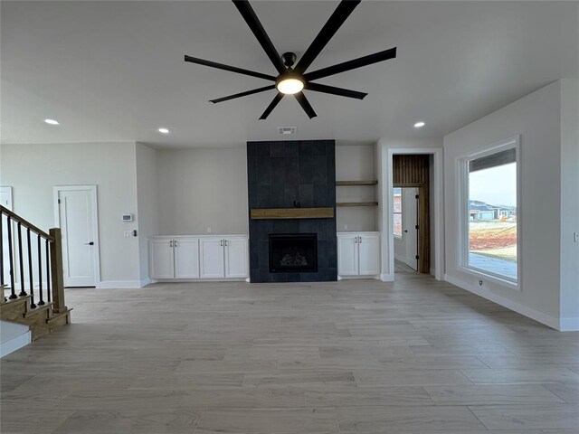 unfurnished living room with ceiling fan, light hardwood / wood-style floors, and a tile fireplace