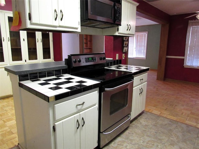 kitchen with light parquet floors, stainless steel appliances, white cabinetry, and tile counters