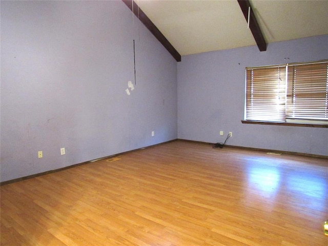 spare room featuring vaulted ceiling with beams and light hardwood / wood-style floors