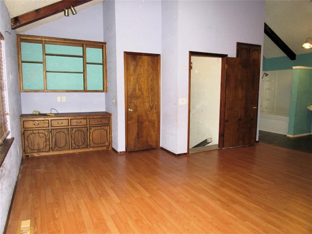 empty room featuring beamed ceiling, light hardwood / wood-style floors, and high vaulted ceiling