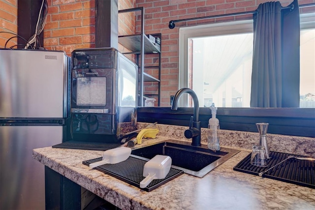 kitchen with brick wall, sink, a wealth of natural light, and stainless steel fridge