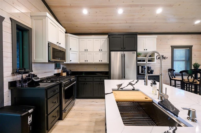 kitchen with stone counters, stainless steel appliances, white cabinetry, and wooden walls